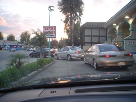 1993 Ford Taurus - Cars wait in line for the car wash entrance under a cloudy sky.