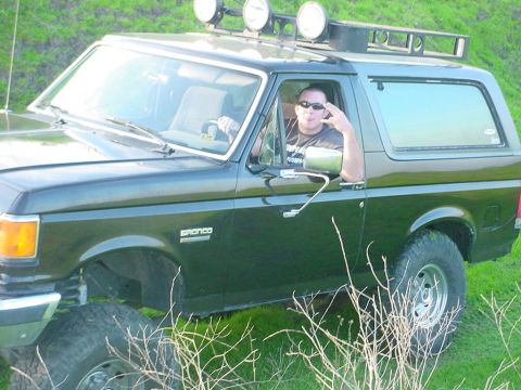 1988 Ford Bronco - A man poses for a photo inside a lifted Ford Bronco parked in a grassy field.