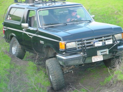 1988 Ford Bronco - 1988 Ford Bronco navigates a muddy, grassy incline with a winch and brush guard attached.
