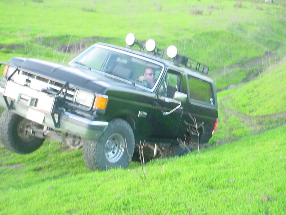 Black Ford Bronco with roof rack and off-road lights driving on a grassy hill