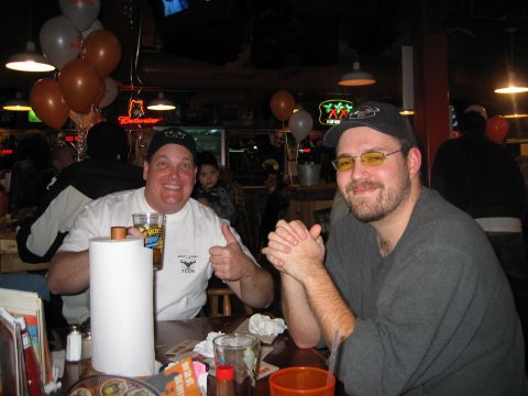 2002 Ford Taurus - Two men enjoy a meal and drinks at a restaurant, with balloons and neon signs in the background.