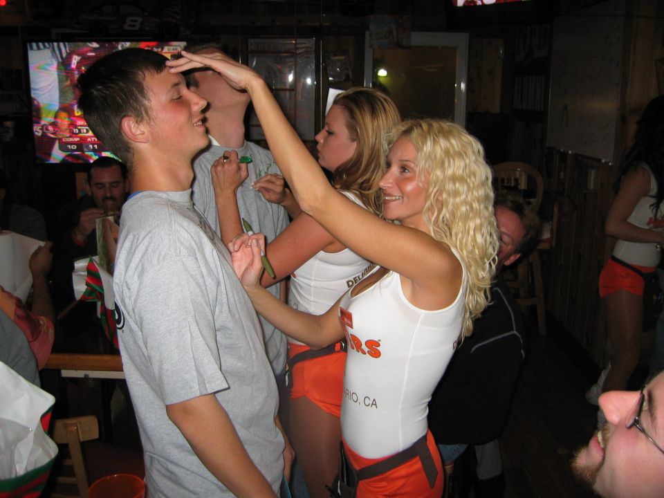 guy getting poked on forehead by woman in Hooters uniform, another woman behind her, people in background