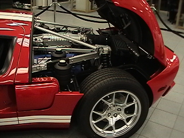 Red sports car engine bay with exposed engine components and white racing stripes on the side