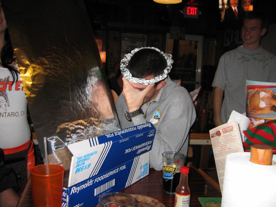 Guy with foil on head, another guy in gray shirt, and a woman in a Hooters shirt at a table with Reynolds Foodservice Foil