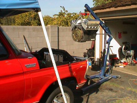 1979 Ford Bronco - An engine is being removed from a red Ford Bronco using an engine hoist in a driveway.