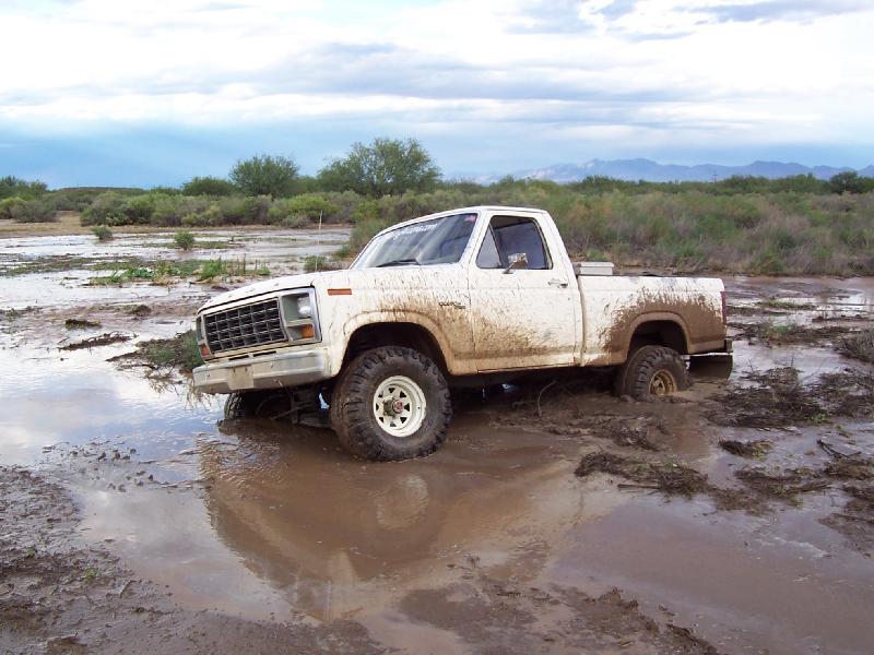 Mud-covered white early-80s Ford F-series 4x4 short-bed stuck in flooded desert mud