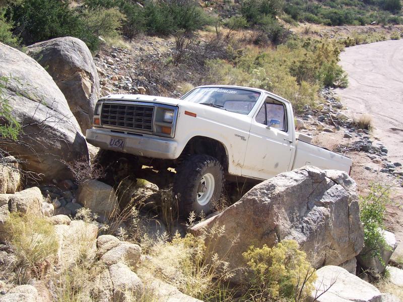 White early-80s Ford pickup crawling over large boulders on a desert trail