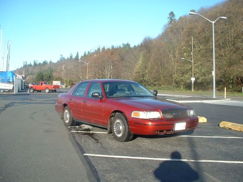 1999 Ford Crown Victoria - A red sedan is parked in a lot with a red pickup truck visible in the background.