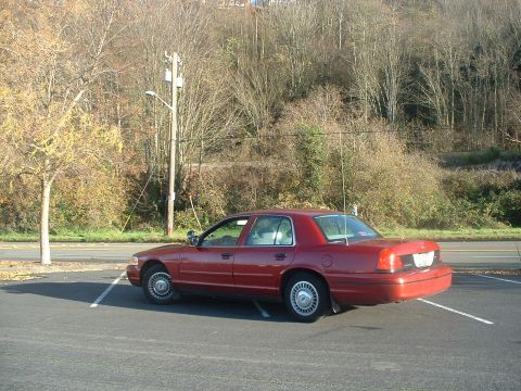 1999 Ford Crown Victoria - A red sedan is parked in an outdoor lot with trees and a utility pole in the background.