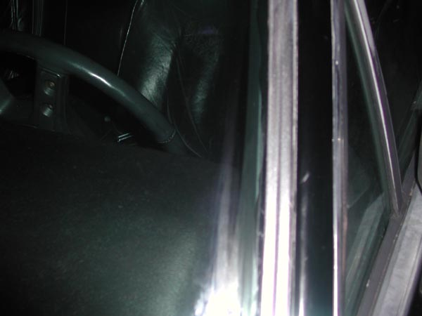 Dark car interior with black steering wheel, leather seat and chrome window trim