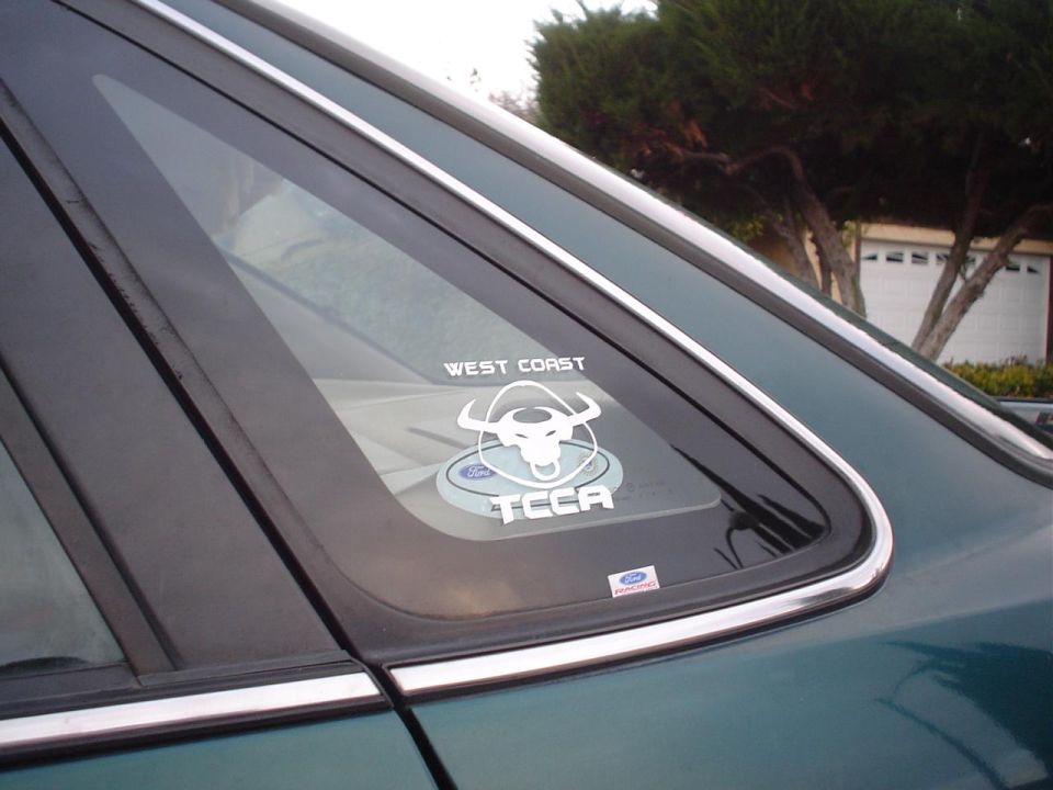 Green car rear window with a "West Coast TCCA" sticker and a Ford logo sticker