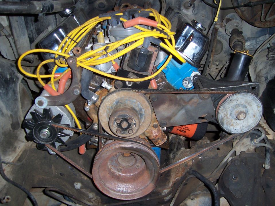 V8 engine front showing alternator, pulleys and yellow plug wires viewed from below