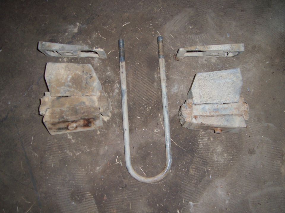 Two rusty leaf-spring perches and a U-bolt laid out on a concrete shop floor