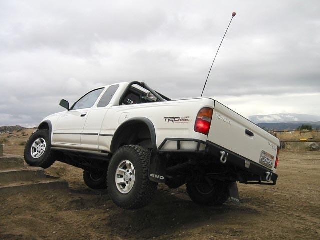 White 1999 Toyota Tacoma TRD off-road pickup truck with large tires climbing over dirt steps