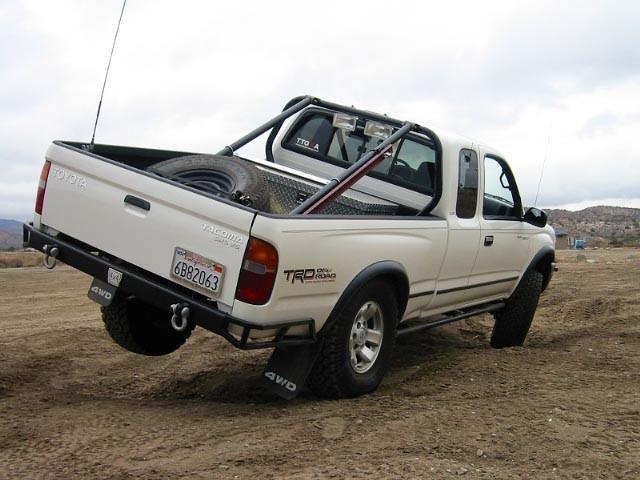 White 1999 Toyota Tacoma pickup truck, rear 3/4 view, with a spare tire in the bed and a roll bar