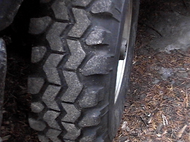 Close-up of a knobby off-road tire on a vehicle. The tread pattern is aggressive, suitable for dirt or mud