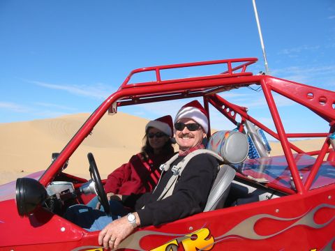 1993 Ford Taurus - Two people in Santa hats enjoy a ride in a red dune buggy through the desert.