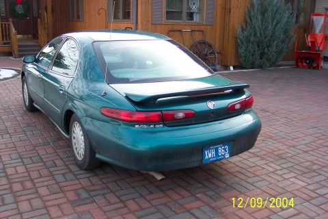 1996 Mercury Sable - The rear of a green 1996 Mercury Sable is parked on a brick driveway in front of a wooden house.