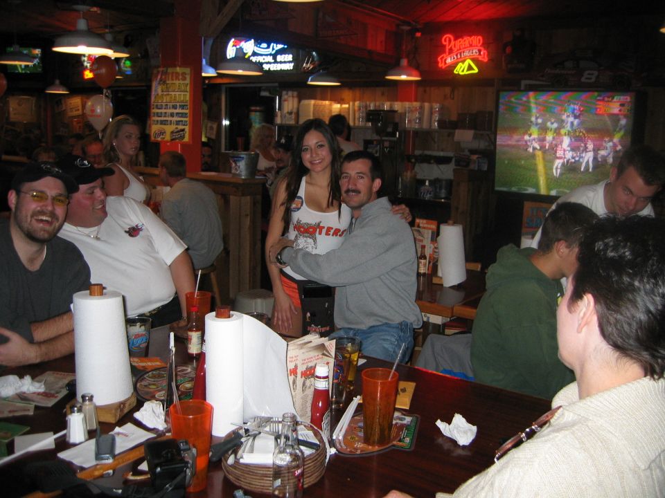 People gathered at tables inside a Hooters restaurant, with a football game on TV