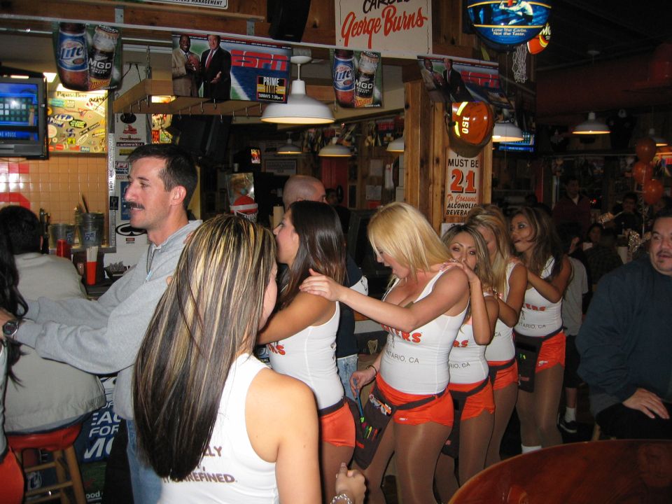 People in a bar with Hooters waitresses in orange shorts and white tops