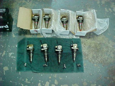 2000 Ford F-250 - Five fuel injectors are displayed on a green cloth, with four additional injectors packaged in boxes in the background.