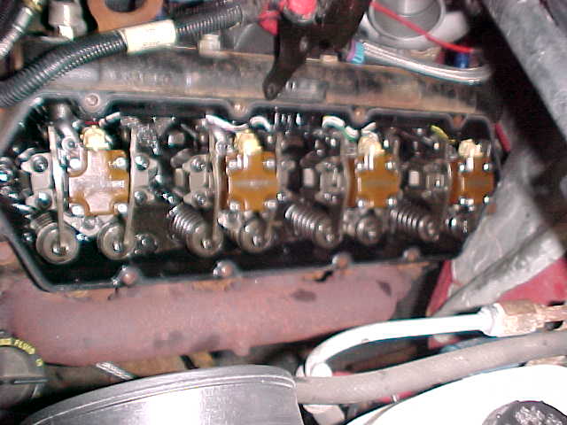 Engine valve train with visible springs and rockers. Rusty exhaust manifold below