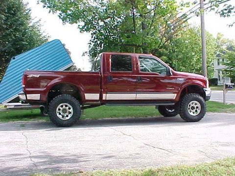 2000 Ford F-250 - A red Ford F-250 truck is parked next to a blue trailer on a sunny day.