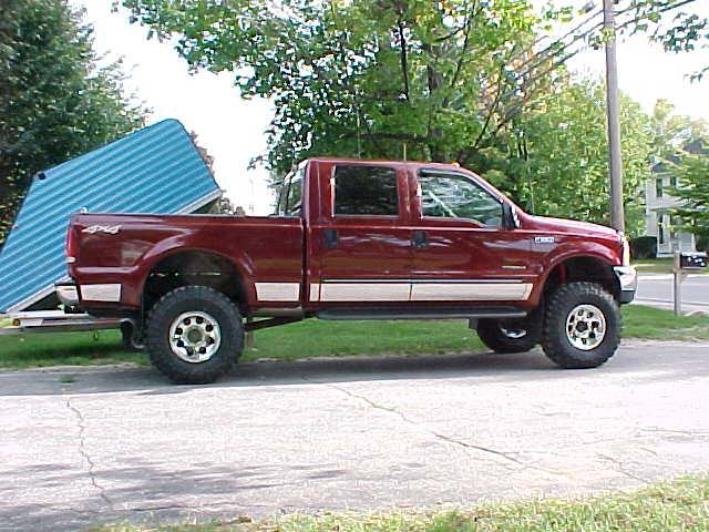 Red Ford F-250 truck, side view, with a blue trailer attached