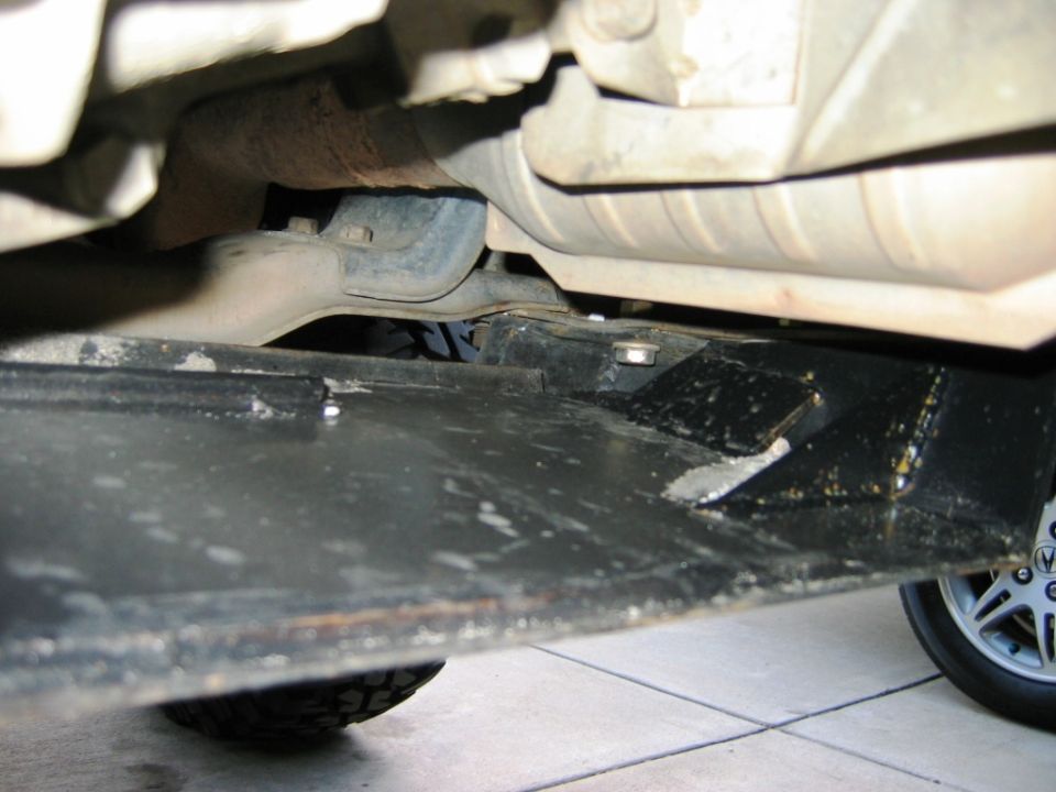 Vehicle undercarriage with black skid plate, exhaust, and suspension over tile floor