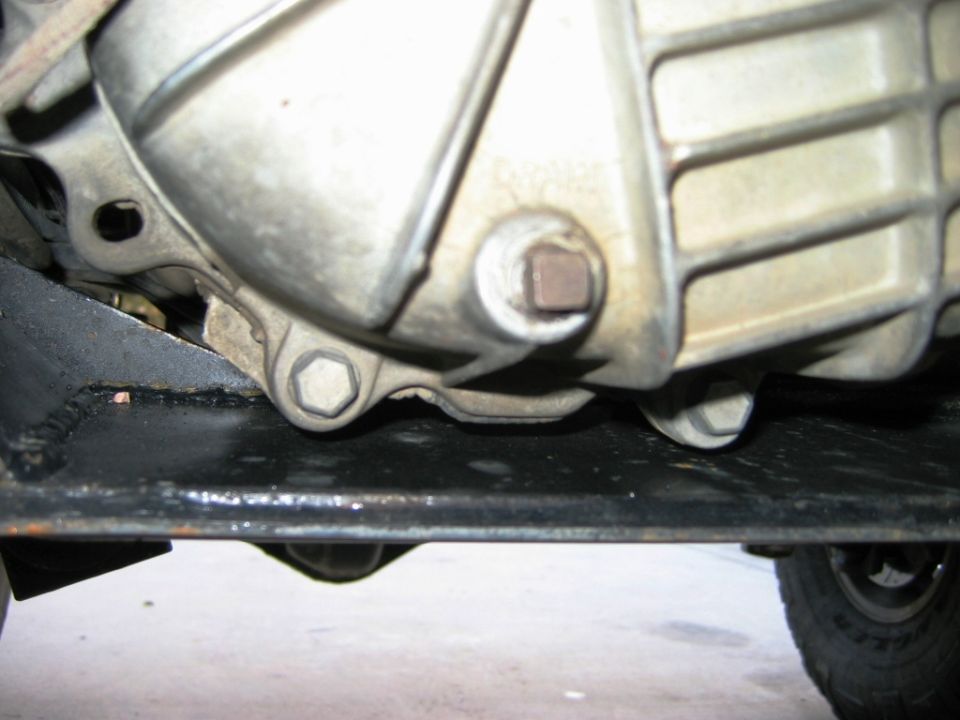 Underbody view of aluminum differential housing with hex and square plugs above black frame rail