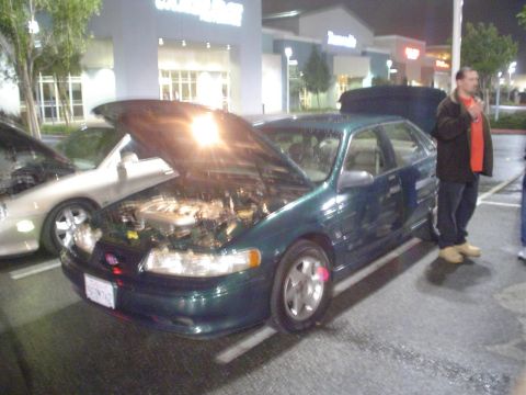 1993 Ford Taurus - A green 1993 Ford Taurus sedan is parked with its hood open, alongside another vehicle.