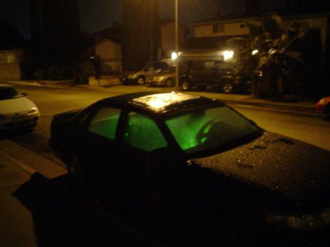 1993 Ford Taurus - A dark sedan with illuminated green interior lights and a wet sunroof is parked on a street at night, with other vehicles visible in the ba…