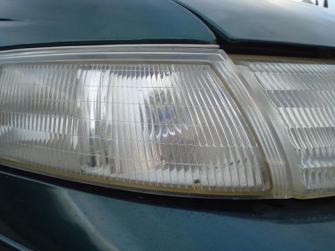 1993 Ford Taurus - The clear plastic headlight assembly shows a ribbed pattern and is mounted on a dark green car body.