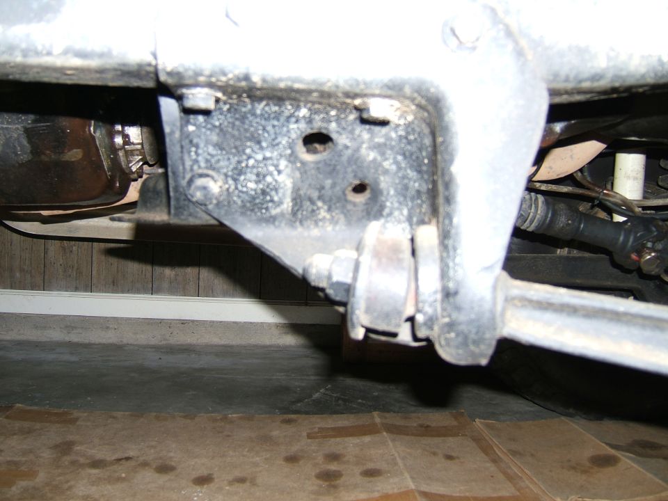 Close-up of a vehicle's suspension linkage and bracket, showing bolts and metal components