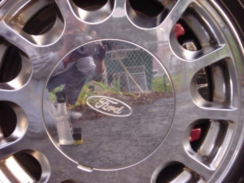 1998 Ford Taurus - A reflection shows a person holding a camera, capturing the shiny Ford logo on the wheel.