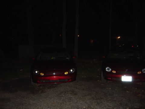 1998 Ford Taurus - Two red sedans are parked outdoors at night, with the one on the left illuminated by its headlights.