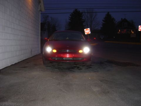 1998 Ford Taurus - Red 1998 Ford Taurus parked in front of a building with headlights illuminated.