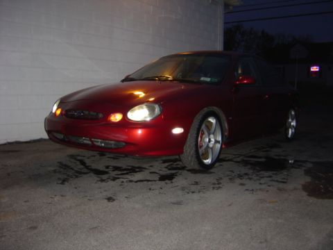 1998 Ford Taurus - A red sedan is parked in front of a brick building at night. The car has custom wheels.