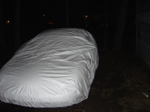 1998 Ford Taurus - A vehicle is completely covered by a white tarp in a dark outdoor setting.