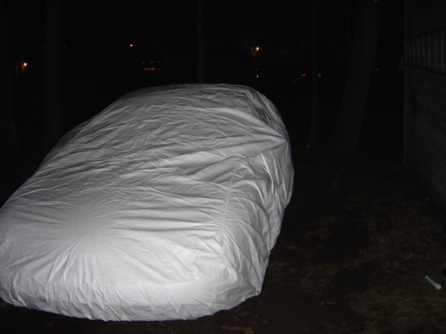 Car covered in a white tarp at night