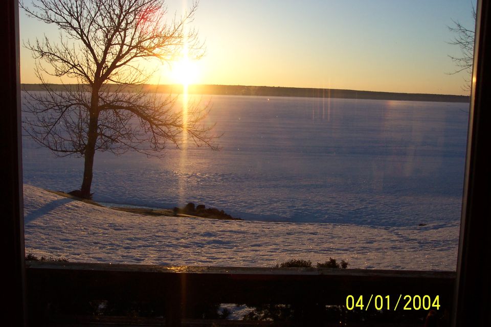 Sunset over a frozen snow-covered lake with a bare tree, seen through a window, dated 04/01/2004