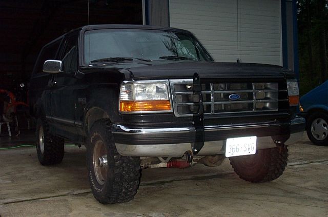 Lifted black Ford Bronco with grille guard and mud tires parked outside a shop, front 3/4 view