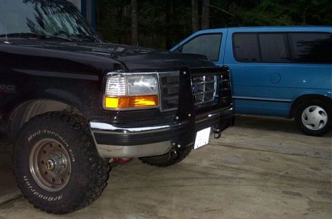 1995 Ford Bronco - Front three-quarter close-up of a lifted black Ford Bronco with a black tube grille guard over the headlights and grille, chrome bumper, an…