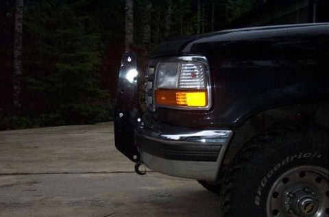 1995 Ford Bronco - Night shot of the driver-side front corner of a black Ford truck/SUV with the headlight and amber turn signal lit, chrome bumper, and a tal…