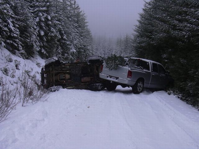 Overturned truck on snowy road next to a silver pickup truck with a Christmas tree in the bed