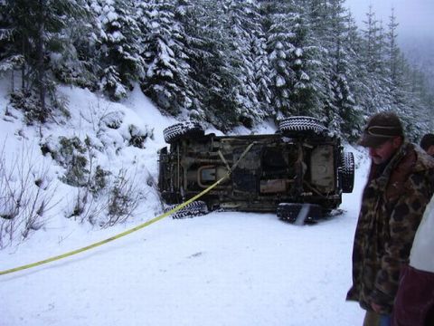 1995 Ford Bronco - A vehicle is being towed after flipping over on a snow-covered road with trees in the background.