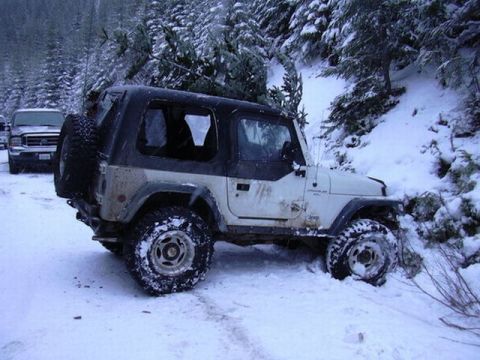 1995 Ford Bronco - A Jeep Wrangler is stuck in the snow while transporting a Christmas tree, with another vehicle visible behind it.