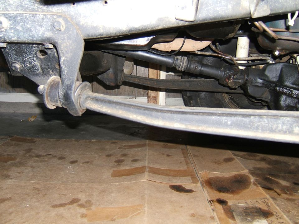 Underside view of a vehicle's suspension and drivetrain components, with oil stains on the floor below