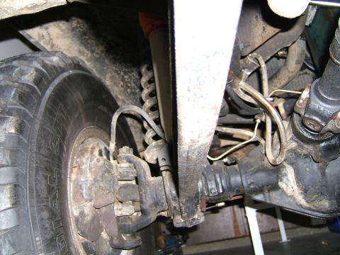 1978 Ford Bronco - Close-up view of the undercarriage, showing the front tire, suspension, and drive axle components of a vehicle.