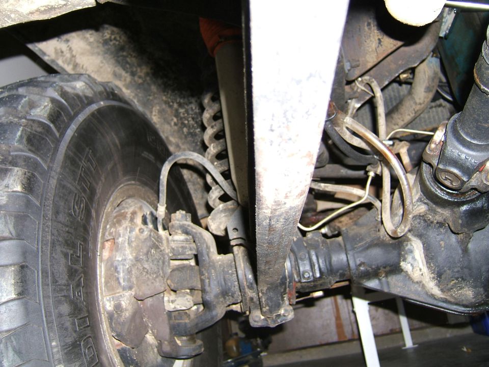 Undercarriage view of a vehicle's front suspension and drivetrain components, including a tire